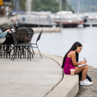A woman sits at the lakeshore and looks through a book.