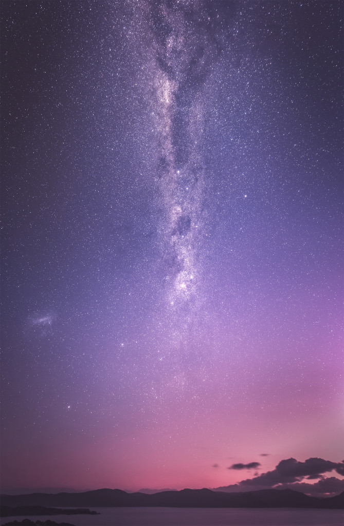 In twilight hues of pinks and purples, the Milky Way galaxy stretches vertically from the horizon to the heavens.