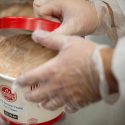 In a close-up phono, a person places a red lid on a container of ice cream labeled 175 S'more Years. The person is wearing clear food safety gloves.