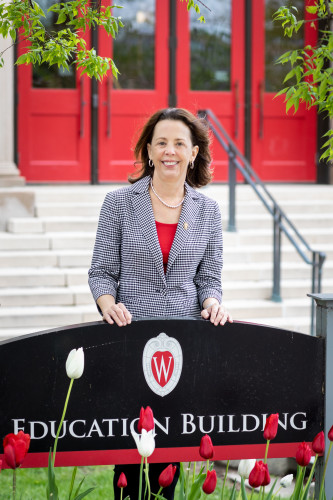 A photo of Diana Hess standing outside the School of Education building's. stone front steps and red doors.