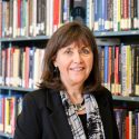 A photo portrait of Erla P. Heyns standing in front of library shelves filled with books.