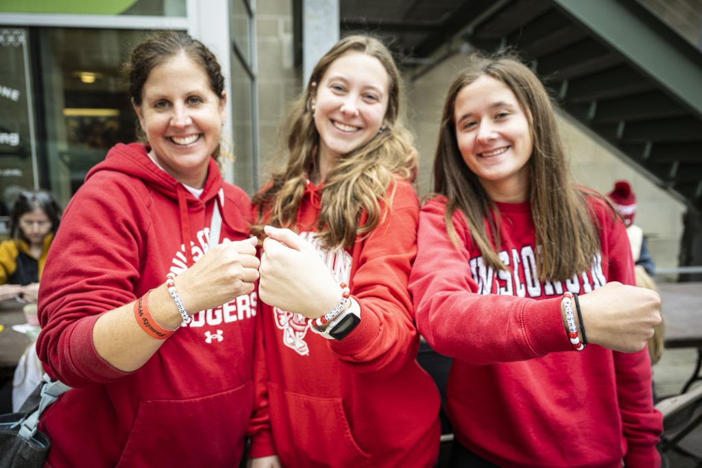 Three women wearing Wisconsin red hold up bracelets.