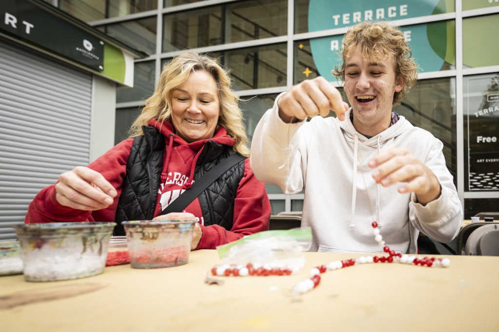 Ryder Ligtenberg and his mother Sara Ligtenberg work on UW-themed jewelry at a Wheelhouse Studios activity booth.