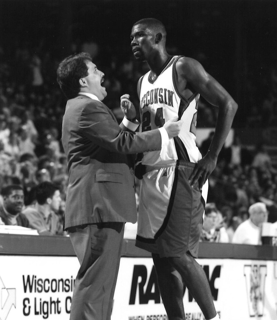 A man in a Wisconsin jersey talks with a coach wearing a suit.