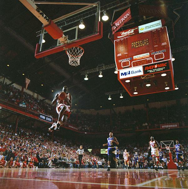 A man leaps high in the air to dunk a basketball at an arena.