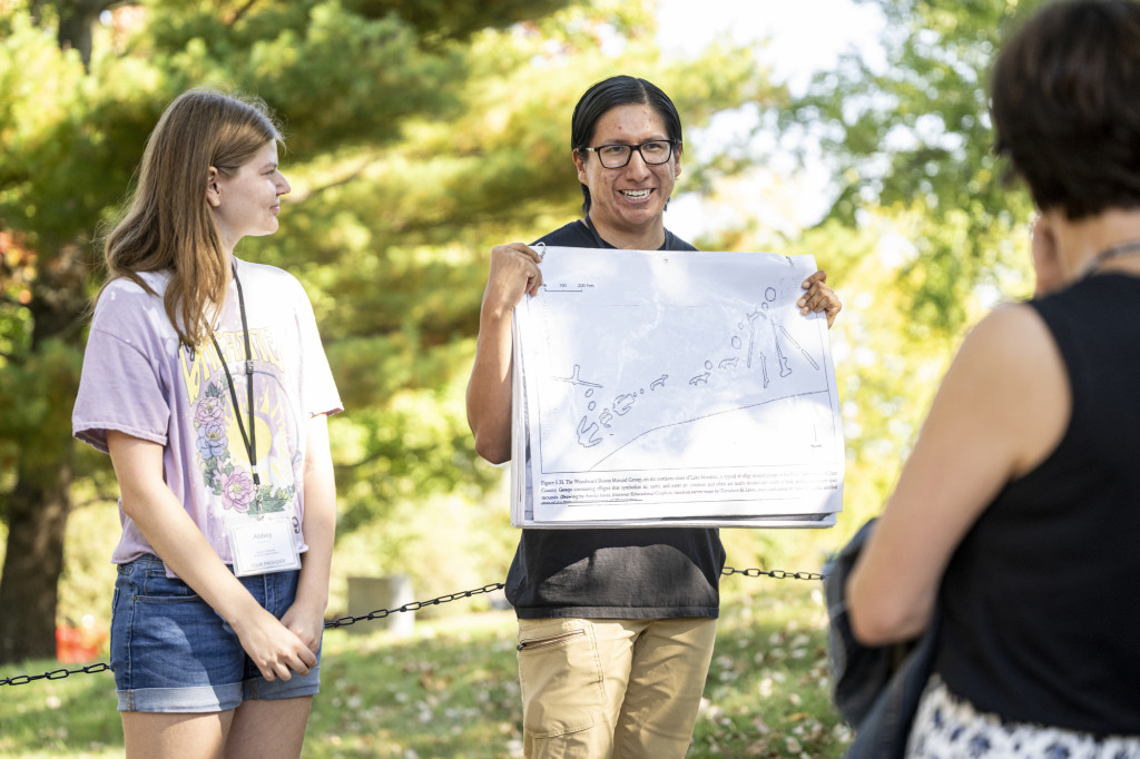 A man holds up a large map showing the locations of effigy mounds on the UW campus. A woman standing next to him looks on as he speaks to a gathered crowd (not seen).