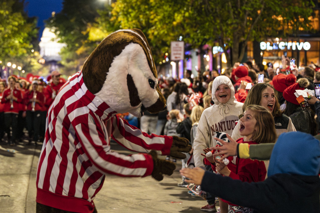Bucky Badger moves in to greet young fans who are cheering and smiling as he approaches.
