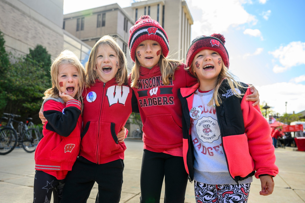 Four young girls wear Badger attire and smile for the camera.