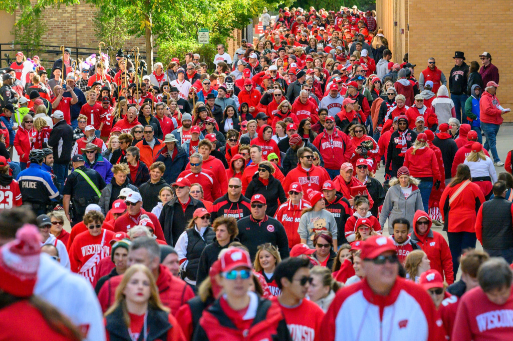 Hundreds of Badger fans wearing red and white attire walk towards the stadium.