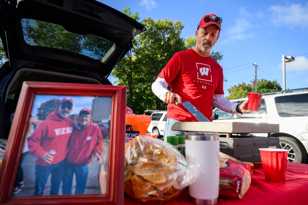 A man in red flips hamburgers on a grill before a football game.