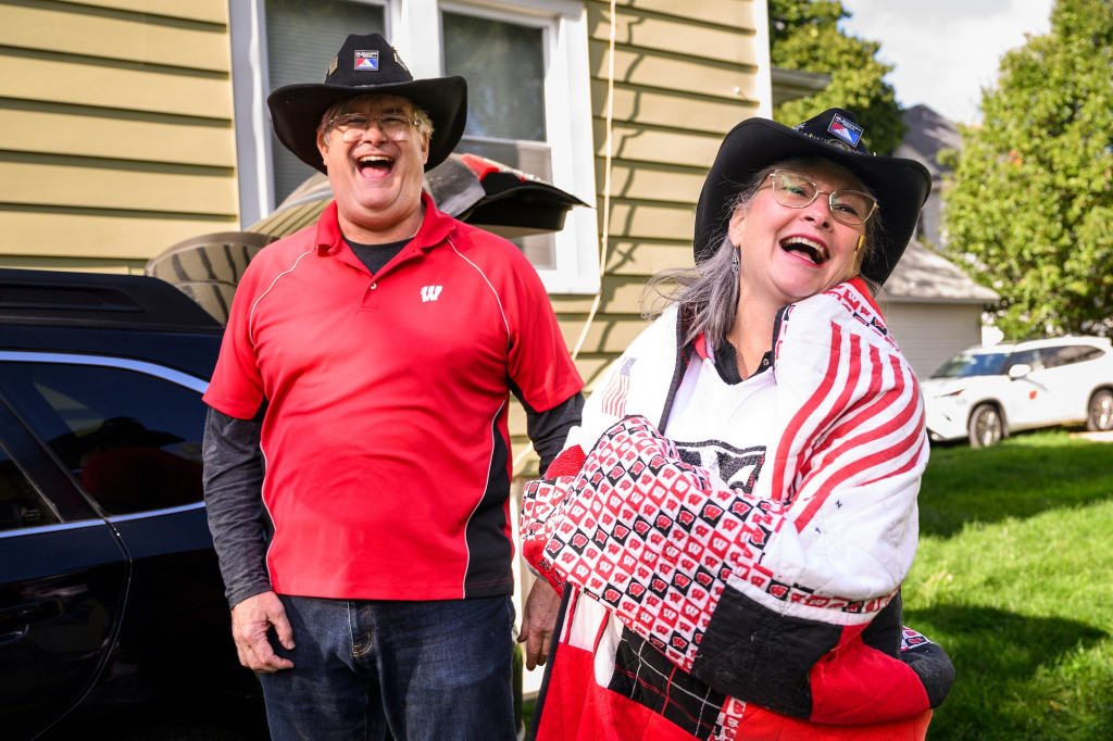 Two fans wearing Badger attire are laughing and enjoying the game day energy outside of the stadium.