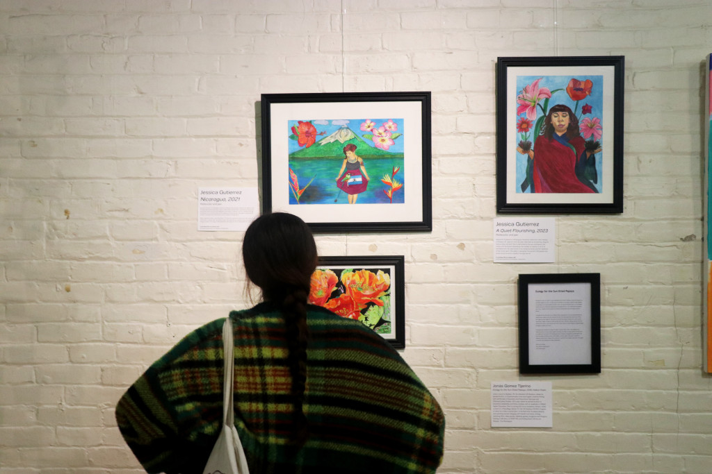 A woman stands in front of an art gallery looking at the art collection hanging on the wall.