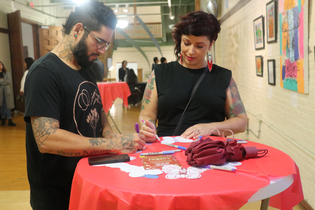 Two people stand at a table and write messages on paper butterflies.