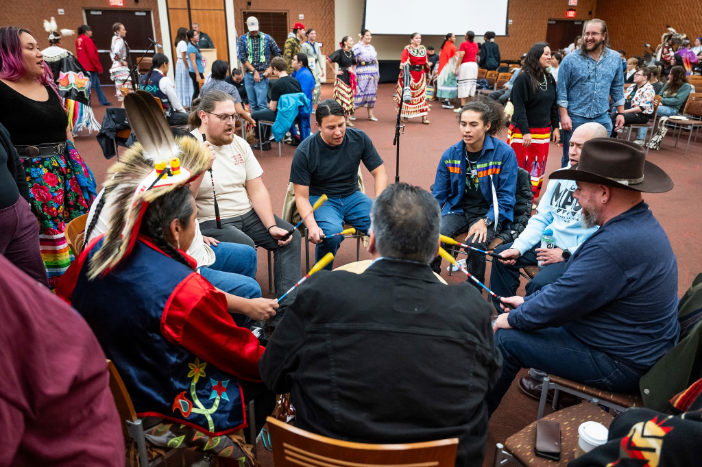 In the middle of the room, a group of eight sit in a circle, singing as they drum.