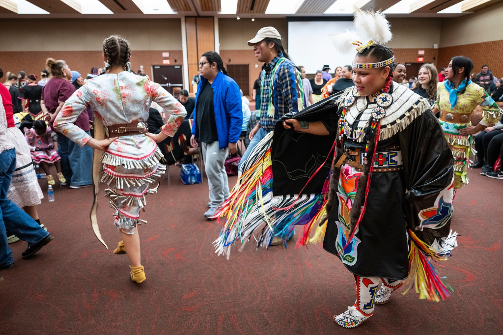 In an open event space, a group of people dance in powwow regalia.