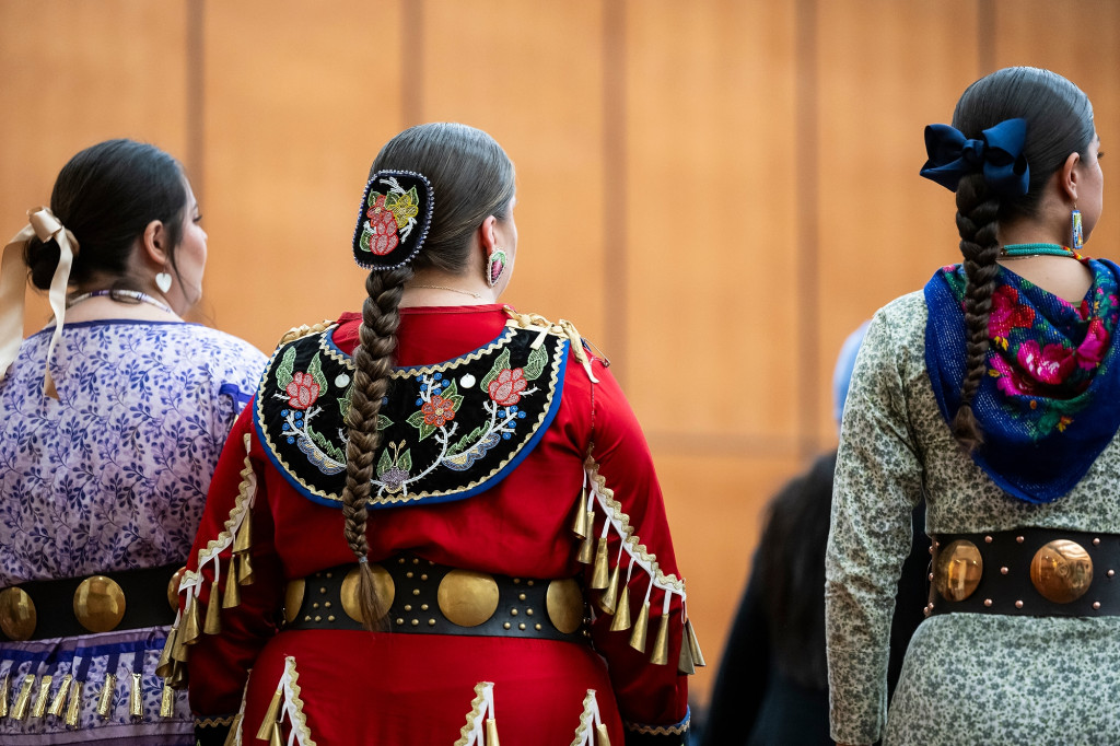 In a photo taken from behind, three women wear regalia adorned with intricate beadwork.