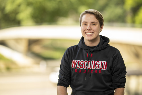 A photo portrait of Tanner Popp wearing a black and red Wisconsin hoodie, sitting outside.
