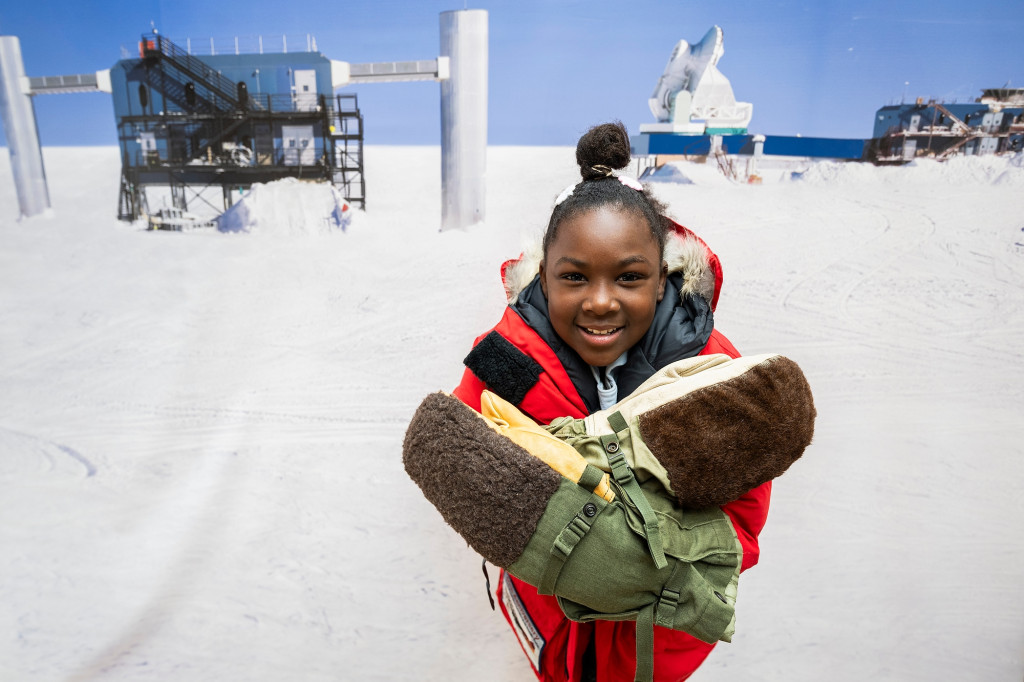 A young girl stands by an exhibit and smiles.