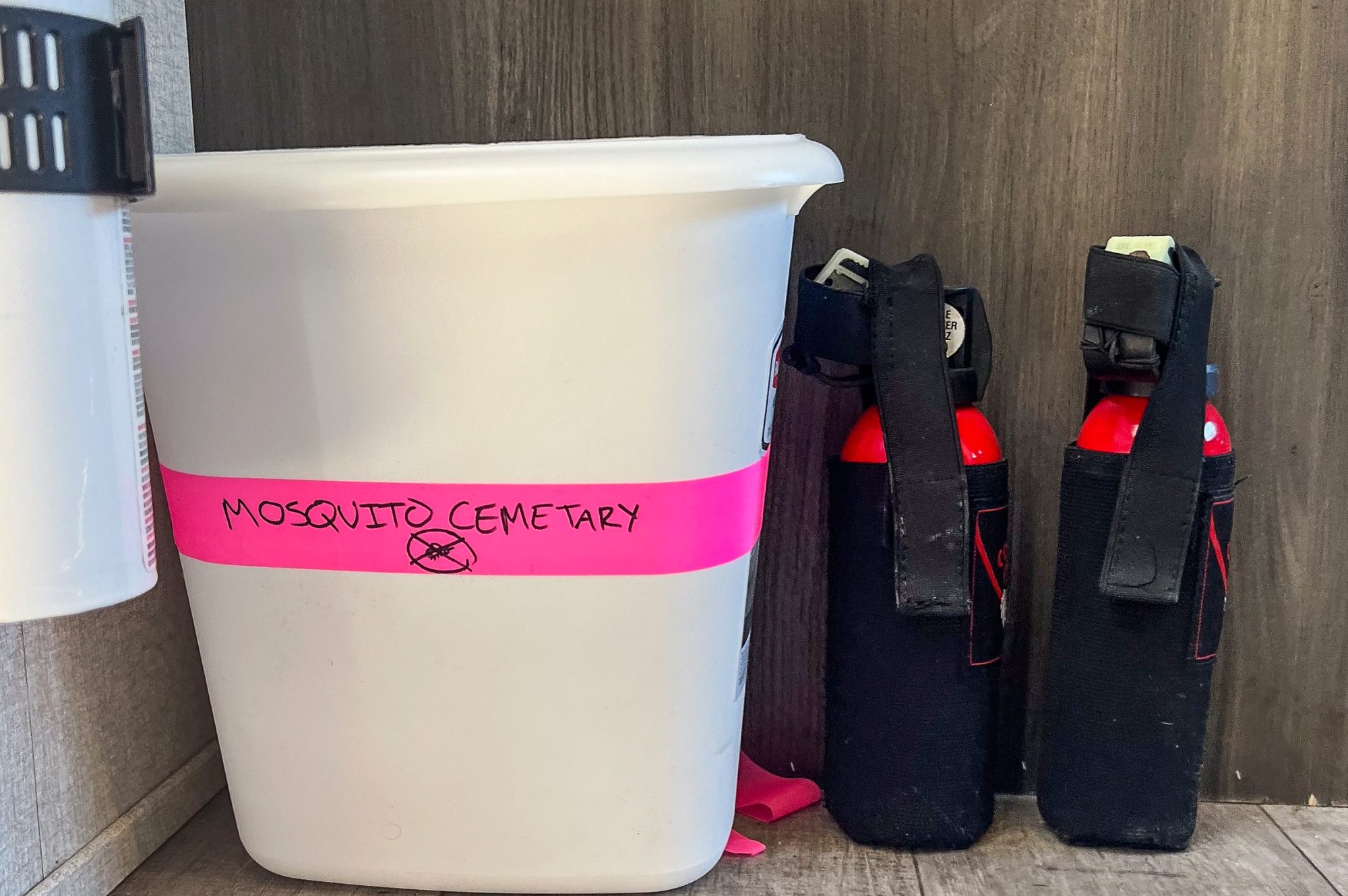 Sitting by the door inside the RV is a plain white trashcan boldly marked by neon pink tape and black sharpie as the "Mosquito Cemetary". Beside the trashcan are two cans of bear spray, sitting idly in their holsters ready to go for the researchers to grab on their way out the door.