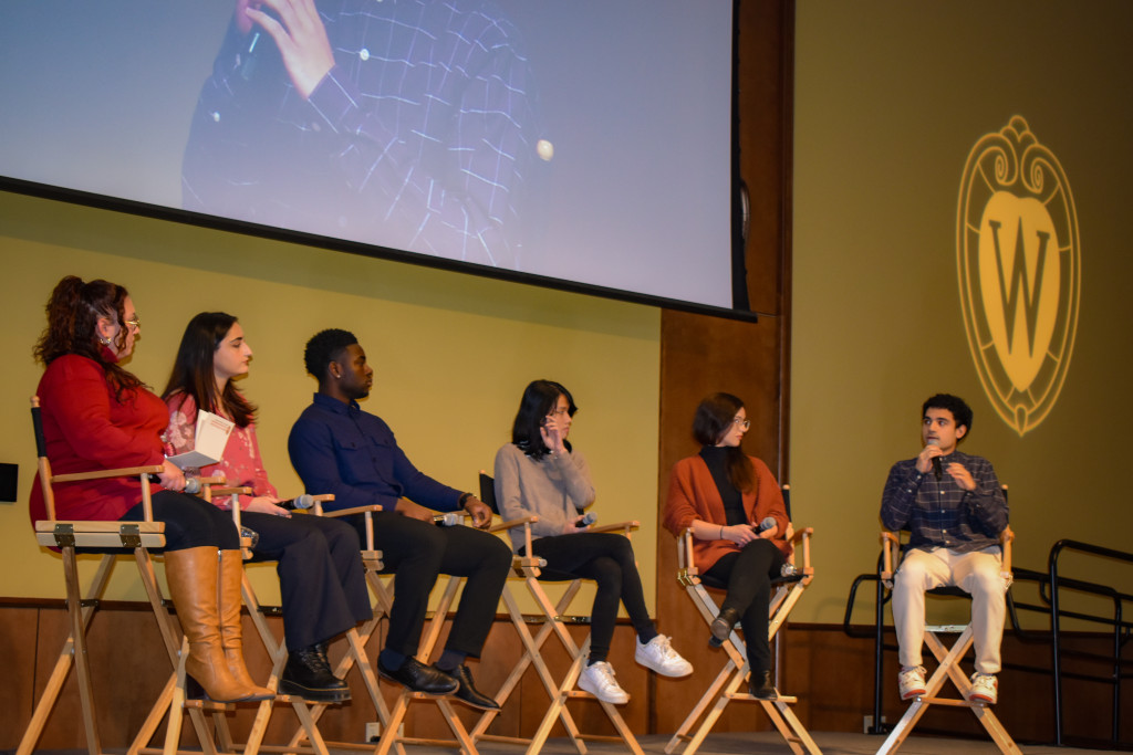 Six people sit in chairs on a stage.