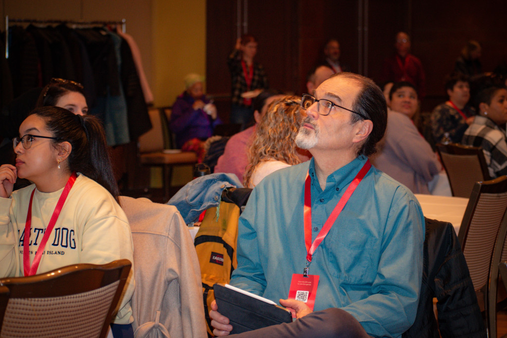 A man in the audience listens to a speech and takes notes.