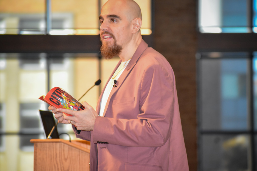 A man standing at a podium holds a book.