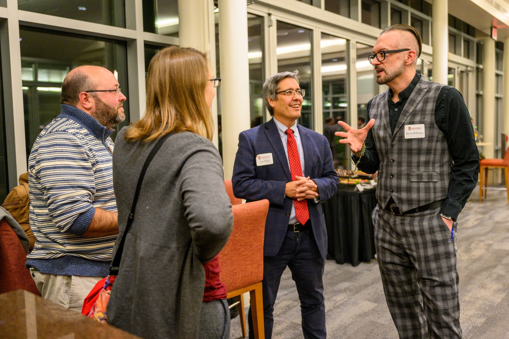 Four people stand around a table and talk.