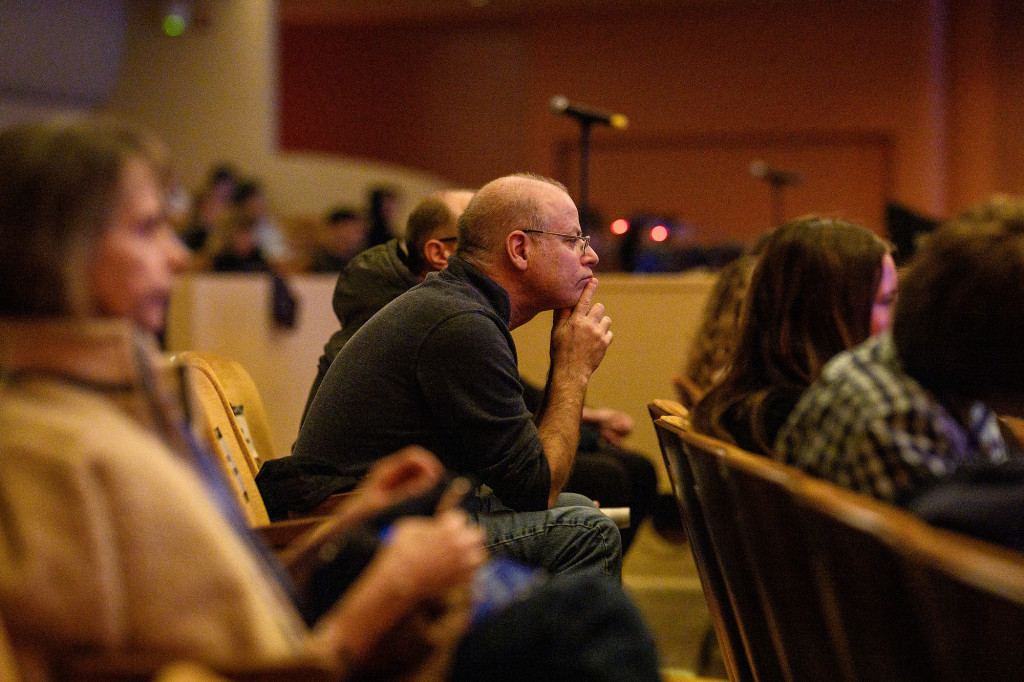 A man leans forward in his chair in the audience.