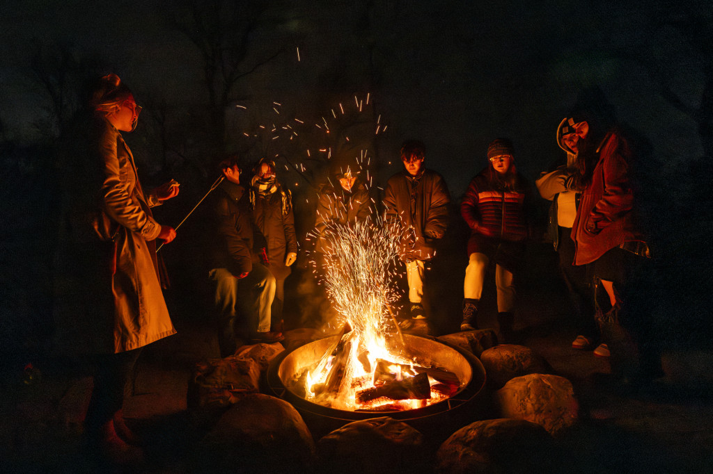 A group of people are shown around a campfire on a dark nightl