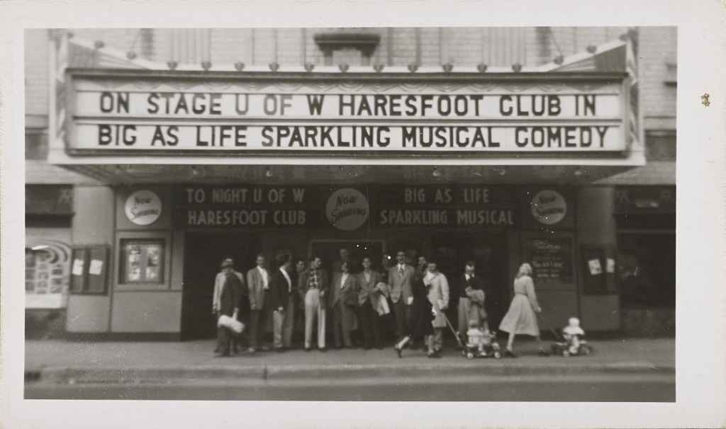 In an old photo, a group of students pose under a theater marquee.