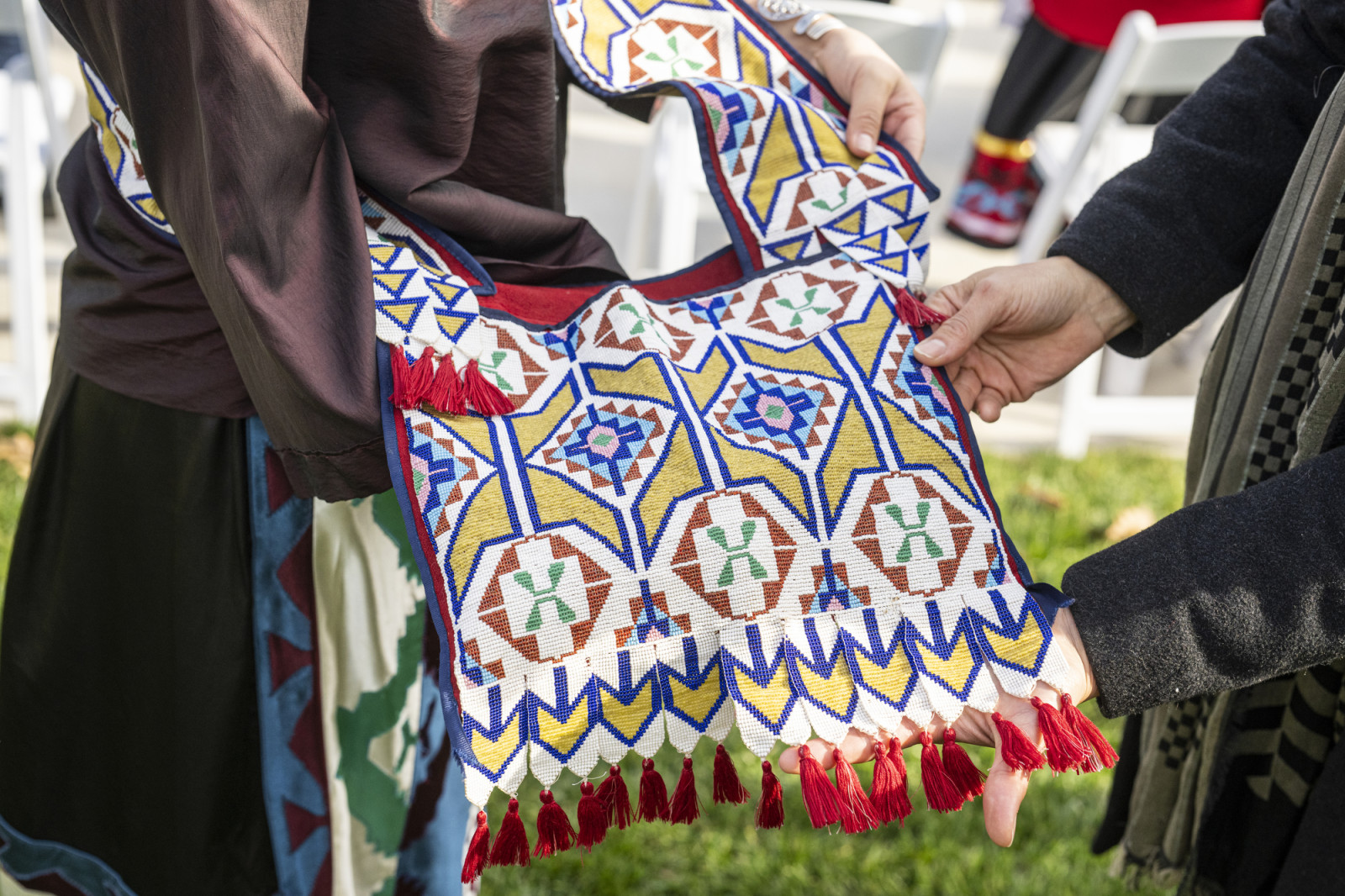 In a close-up photo, a woman holds up an intricately beaded bag in shades of white, blue, yellow, red, pink and orange.