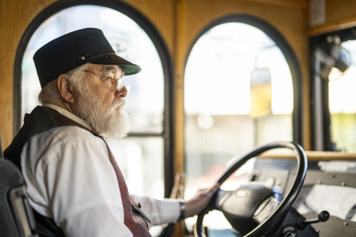 A man in a train conductor-style hat drives the bus.