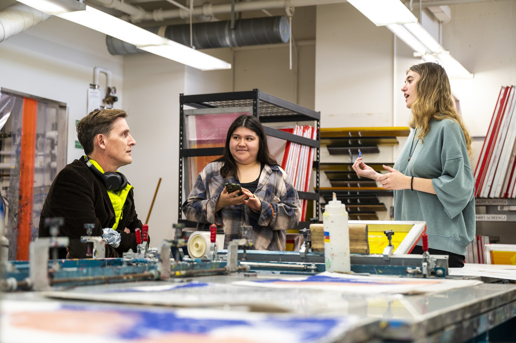 Herrmann (right) and  MFA graduate candidate Jackelin Espinosa Moyotl (center) talk to a visitor about the screen printing process.
