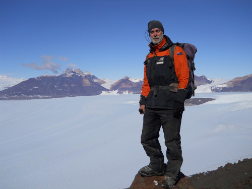 A photo of Richard Levy wearing mountaineering gear and standing in front of a large ice floe.