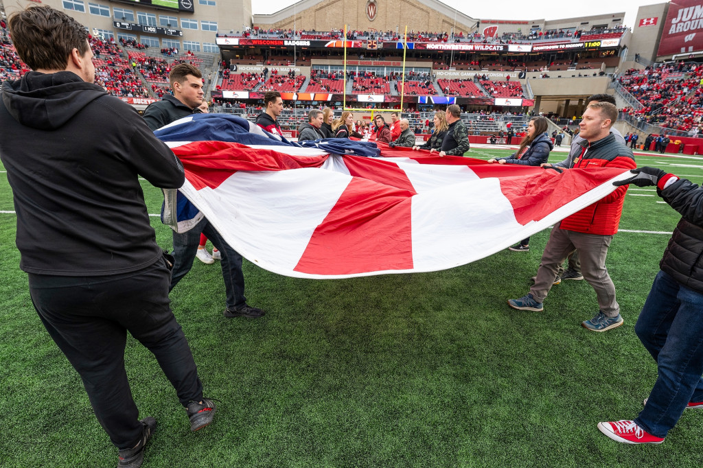 People carry in a giant U.S. flag onto the field at Camp Randall stadium during the first quarter of a football game.