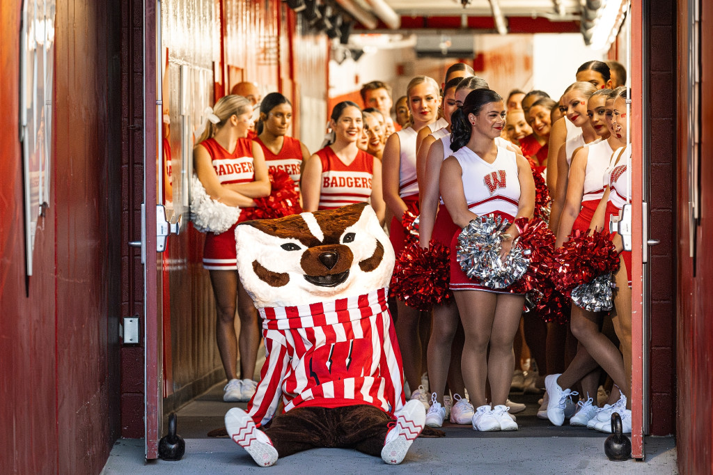Members of the UW Spirit Squad stand in the doorway of an entrance onto the field at Camp Randall. Bucky Badger sits on the ground in front of them.