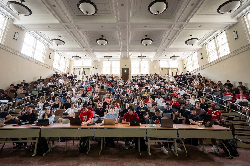 In a stadium-style lecture hall, students fill the seats as they look forward listening to a lecture.