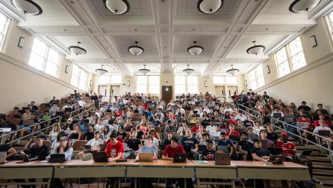 In a stadium-style lecture hall, students fill the seats as they look forward listening to a lecture.