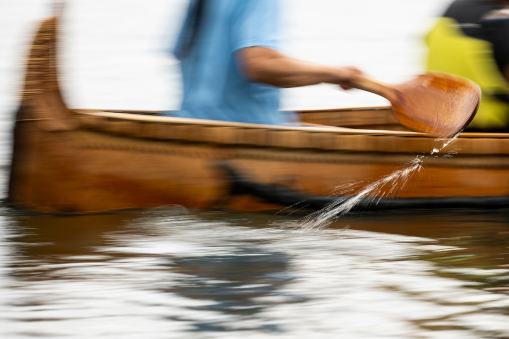 In a blur of motion, a birchbark canoe glides through the water. A stream of water flows off the wooden paddle as the canoer in the back of the craft takes a stroke.