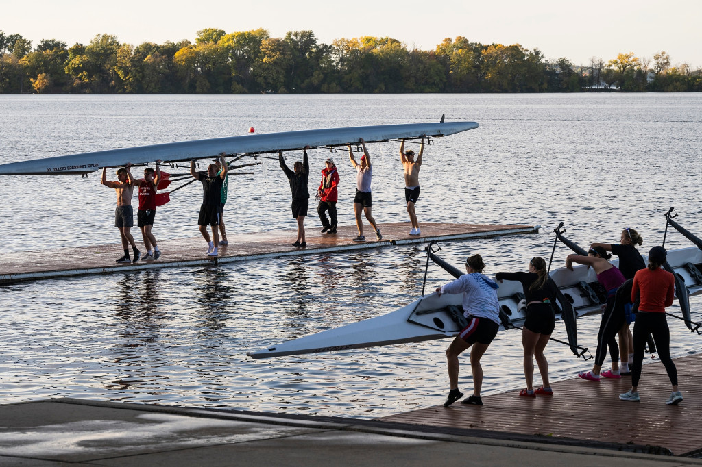 Two groups of people stand on adjoining piers on Lake Mendota. They're lifting crew boats out of the water and overhead to carry them back to the boathouse.