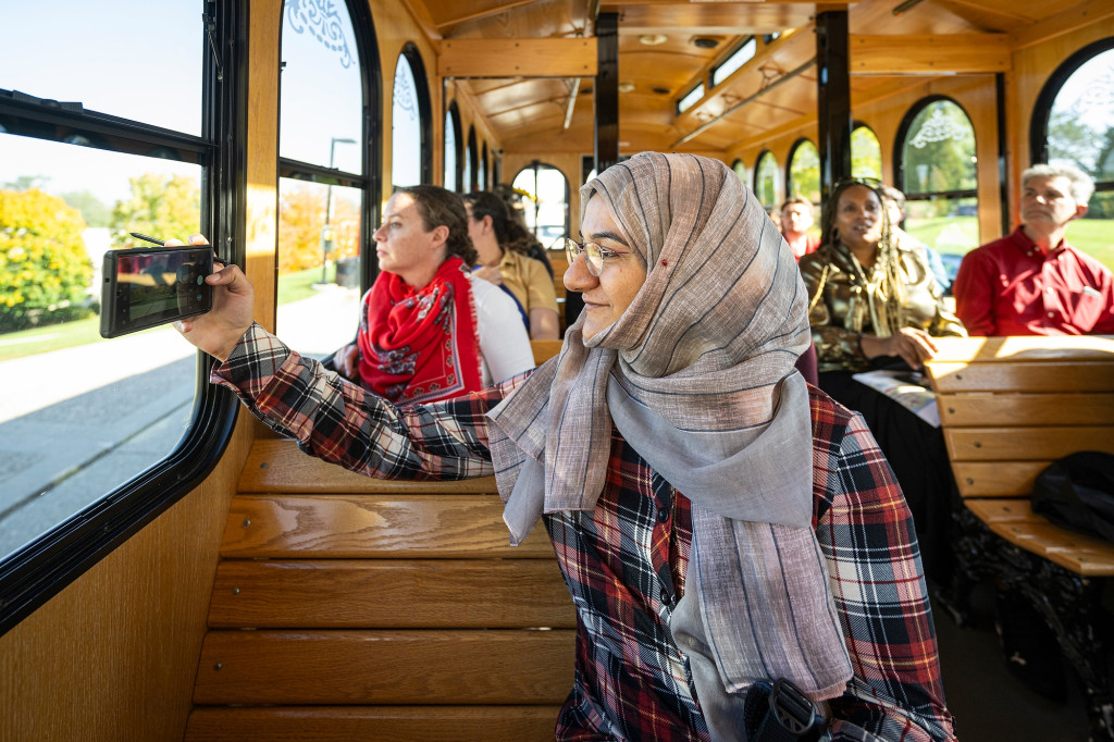 Passengers on a trolley-style bus look out the windows as they tour the UW campus. One woman uses her phone to take photos.