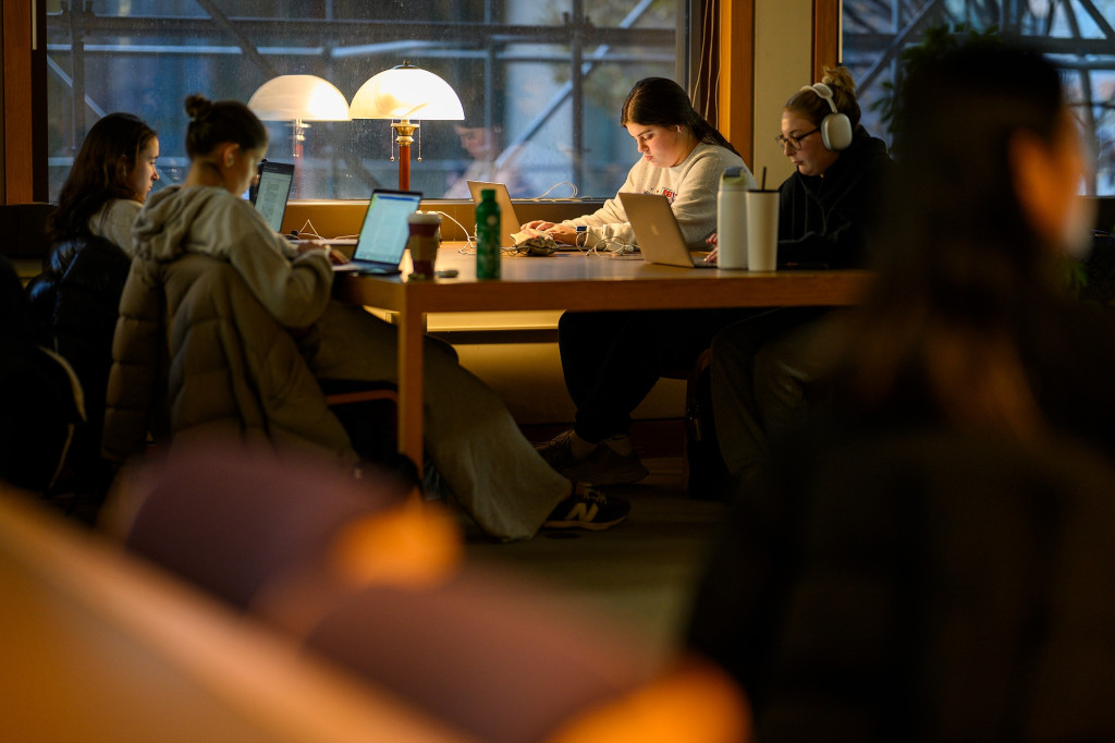 A group of people study around a large wooden table in a softly lit room of the Kohler Art Library.