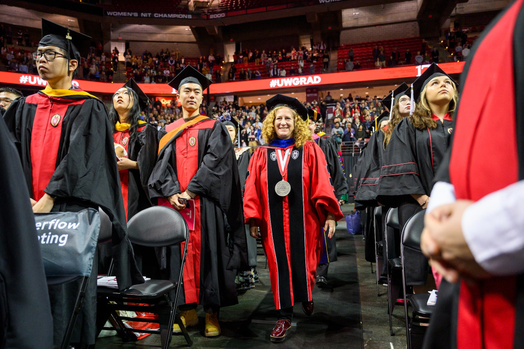 People walk up the aisle in an arena wearing academic robes.