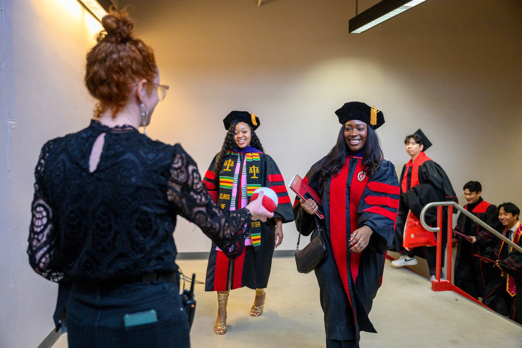 A woman hands out basketballs to people in graduation robes.