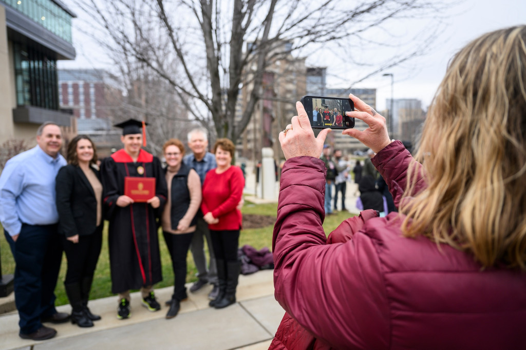 Someone takes a cell phone photo as a family poses together with a person in graduation robes.