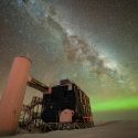A view of the IceCube Lab with a starry night sky showing the Milky Way and green auroras.