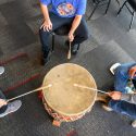 Members of Twin Tails Singers, from left to right, Elias Fox Baker, undergraduate linguistics major, member of the American Indian Science and Engineering Society, and member of the Colville Tribe; Michael Williams, citizen of the Oneida Nation and UW law student; and Silas Cleveland, undergraduate student and Ho-Chunk Nation citizen; drum and sing during the Indigenous alumni social in the Alumni Lounge in the Pyle Center at the University of Wisconsin–Madison on Nov. 18, 2023. (Photo by Althea Dotzour / UW–Madison)