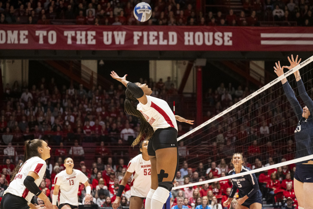 A woman jumps high in the air and arches her back to slam the volleyball.