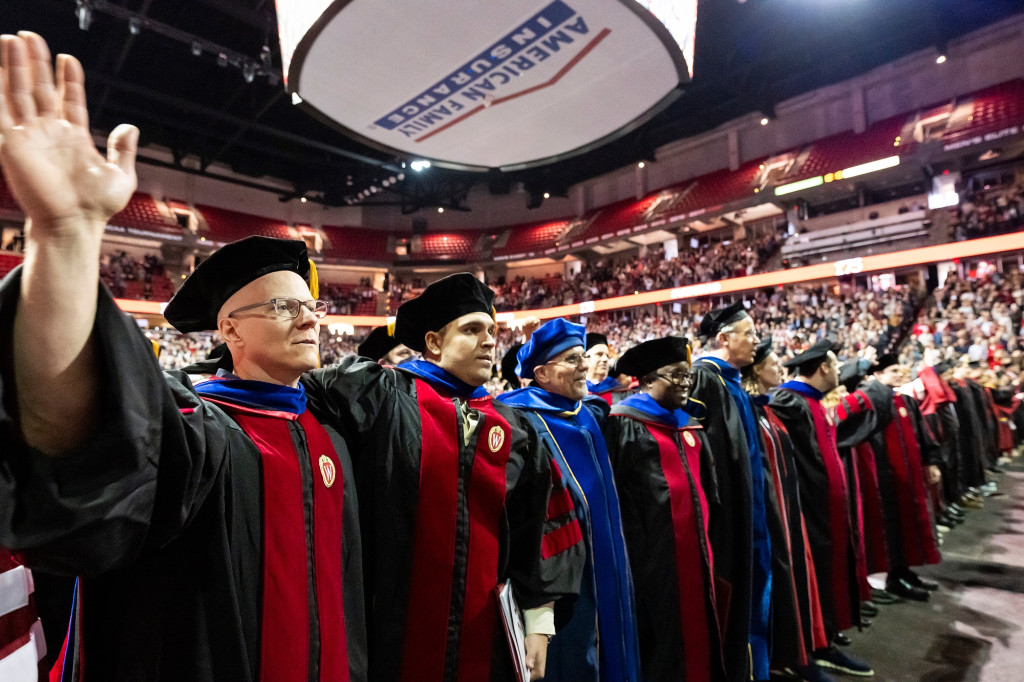 People in academic robes link arms and sing.