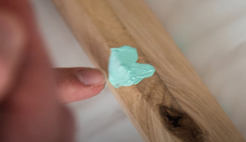 In a close-up ohoto, a finger pulls away from a piece of wood to reveal a fingerprint left behind in light green paint.